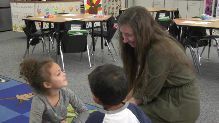 A kindergartner having an aha moment during pair and share, beaming as her teacher leans in